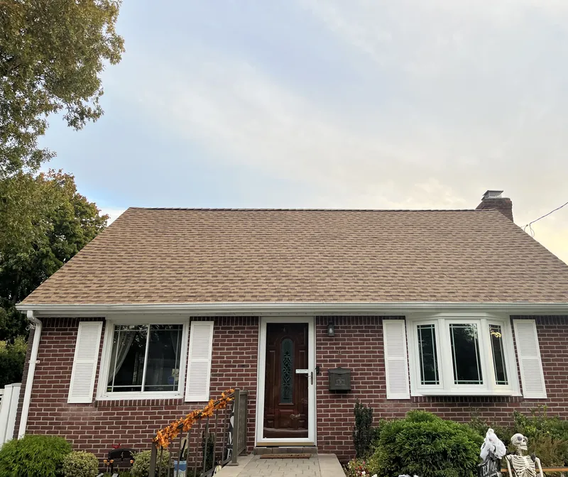 Brick cape house with a new tan shingle roof, white gutters and shutters, and a brick chimney.