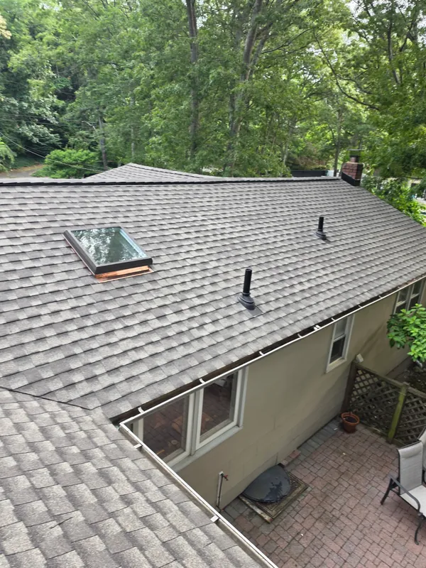 Gray shingle roof with a skylight and two pipe vents, viewed from above, with trees around the house.