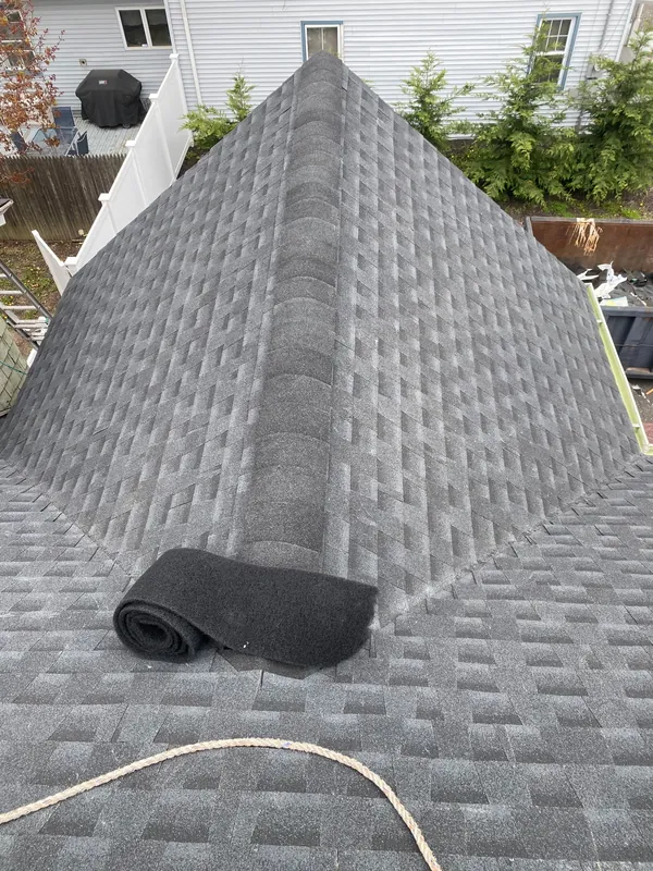 Hip ridge on a gray shingle roof with a roll of ridge vent lying on the slope.