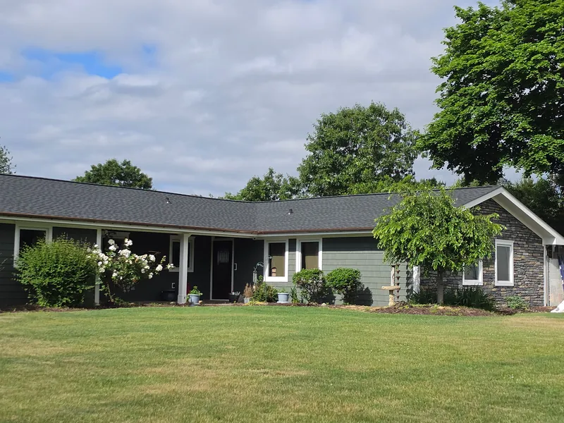 One-story house with a new dark shingle roof, a green lawn in front and trees behind.