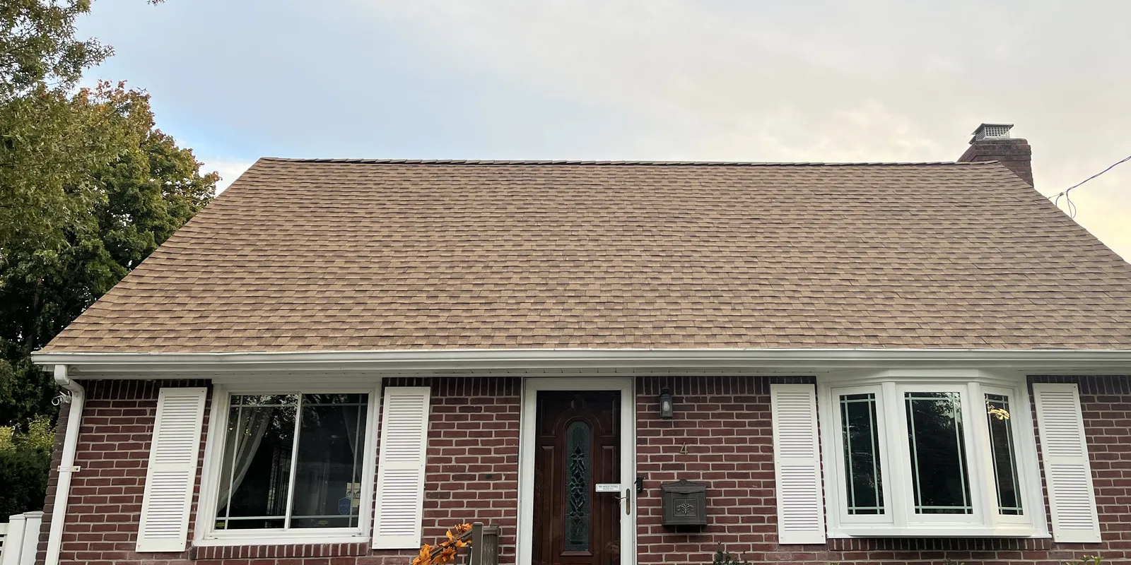 Same brick cape house with its new tan architectural shingle roof